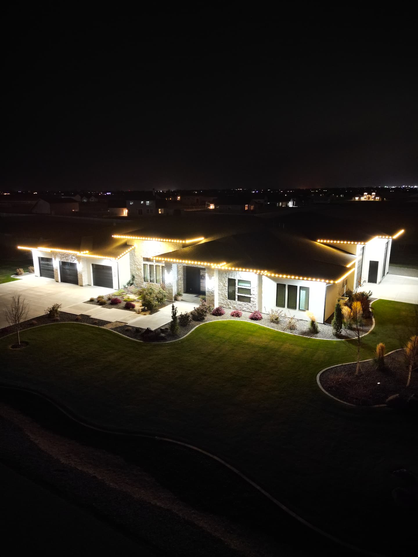 Aerial view of a home outlined with warm white Christmas lights after dark