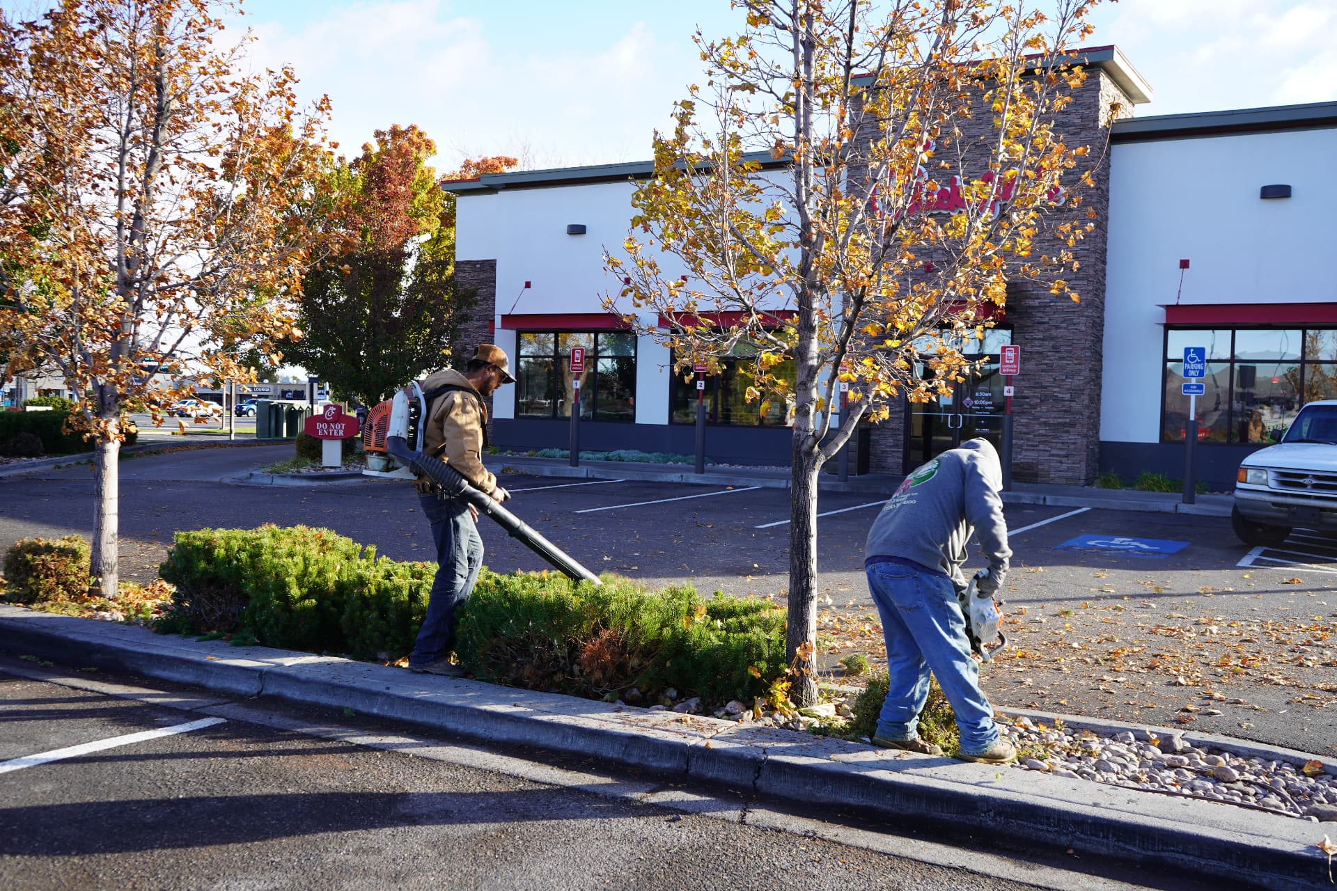 Two Hanks crew members blowing off hedges and curbs at a commercial property