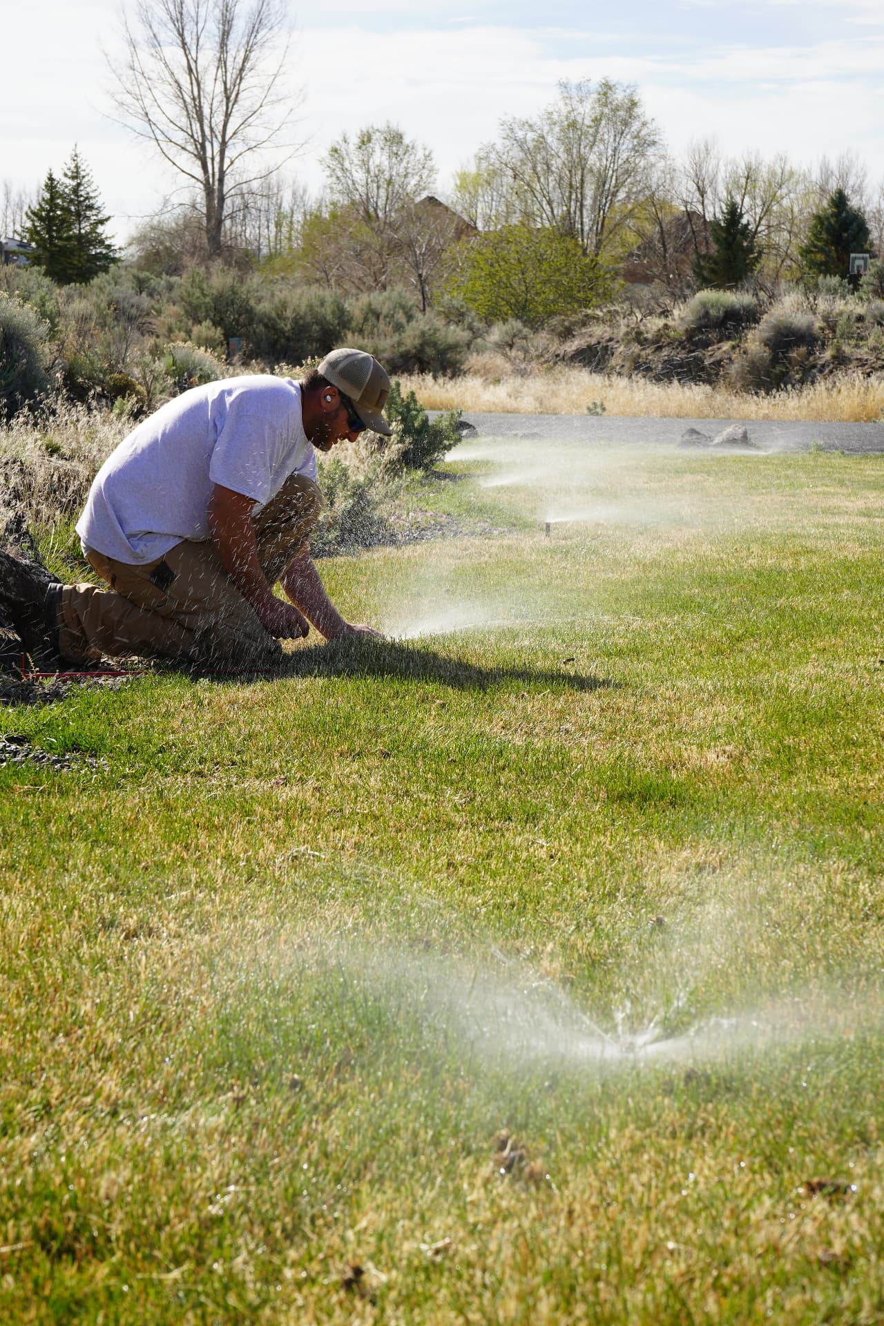 Hanks technician kneeling to inspect and adjust a sprinkler head