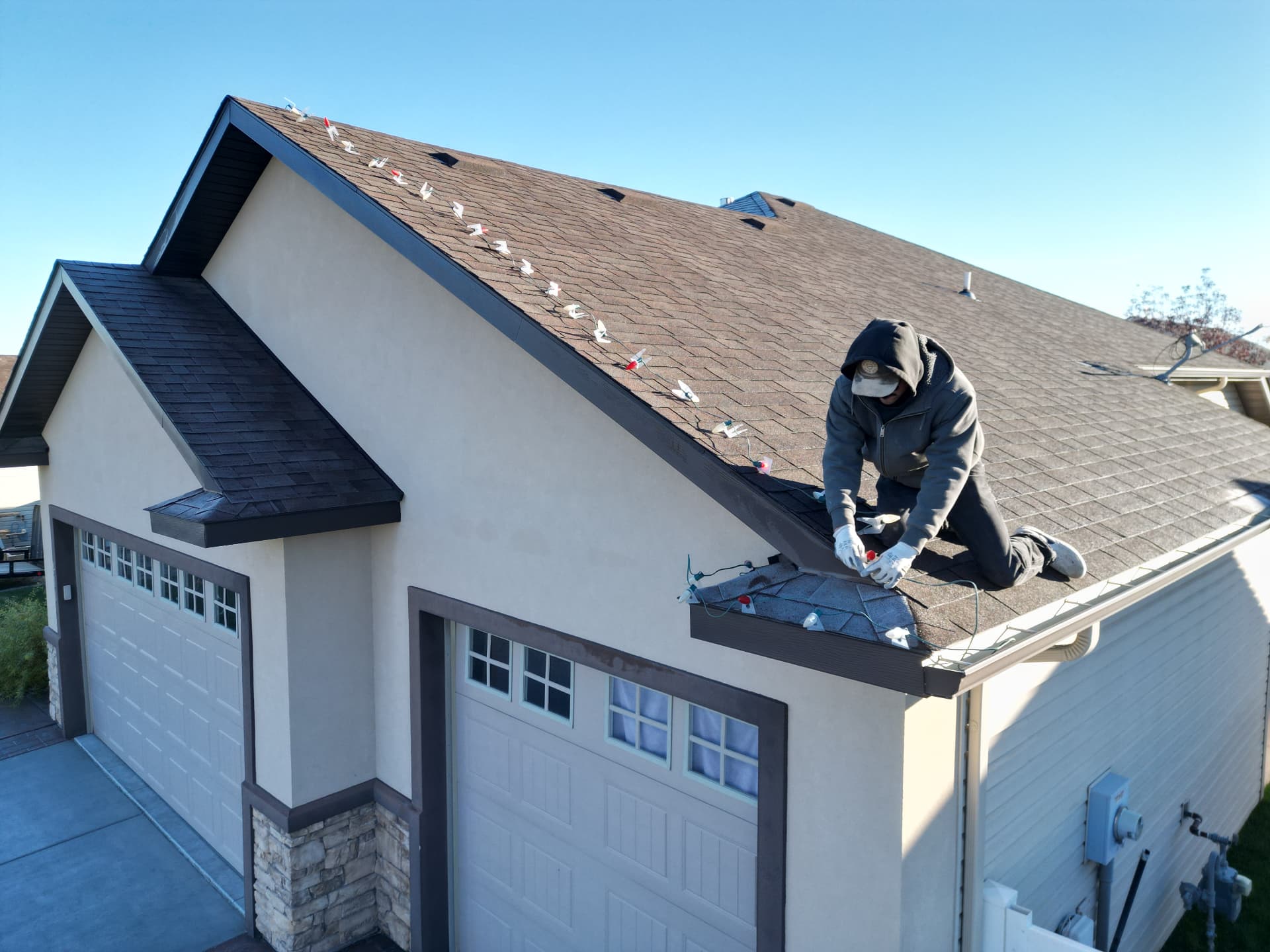 Team member clipping Christmas light mounts along the roofline of a tan home