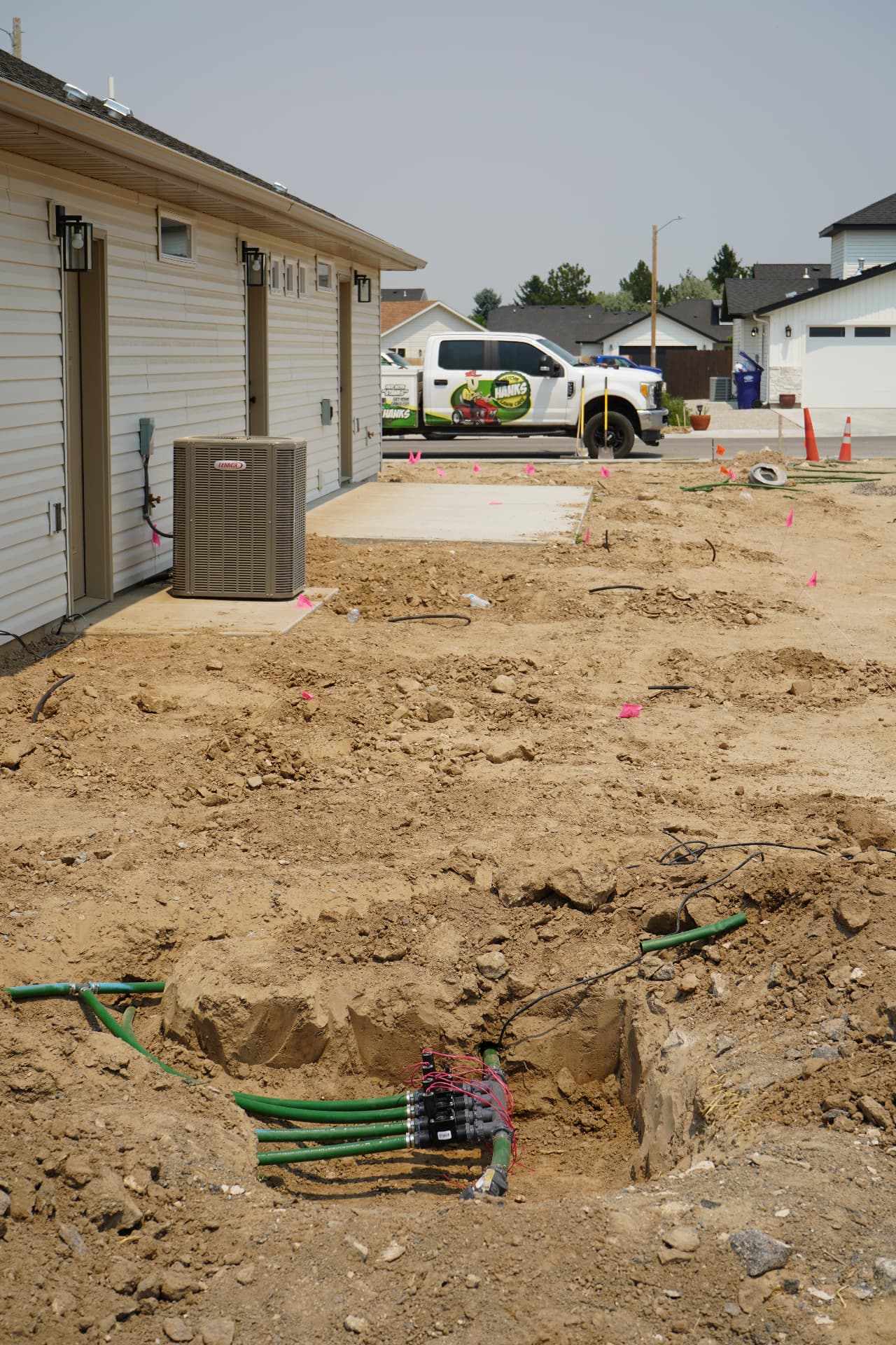 Exposed sprinkler valve box with green PVC pipes and the Hanks truck in the background