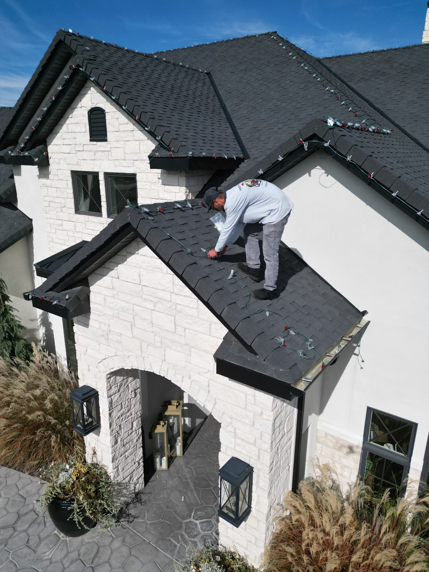 Hanks crew member on a roof installing red and green Christmas lights above a stone entryway