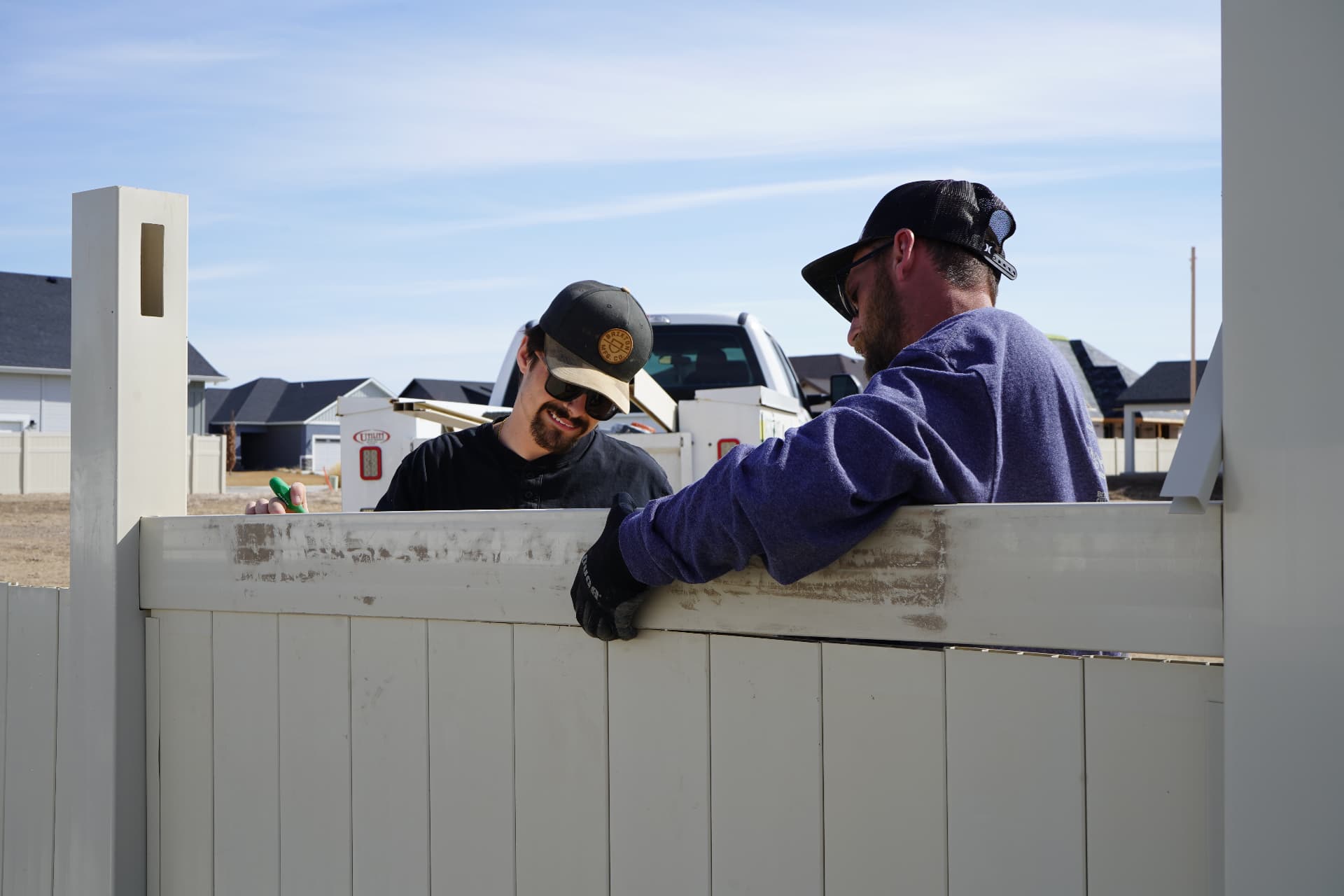 Two Hanks crew members installing a white vinyl privacy fence