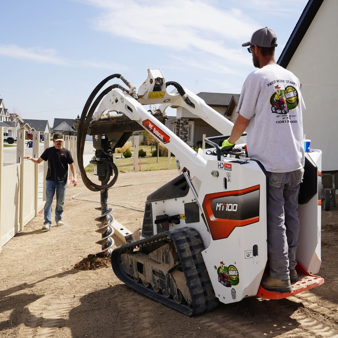 Hanks crew drilling fence post holes with a Bobcat auger while another worker sets posts