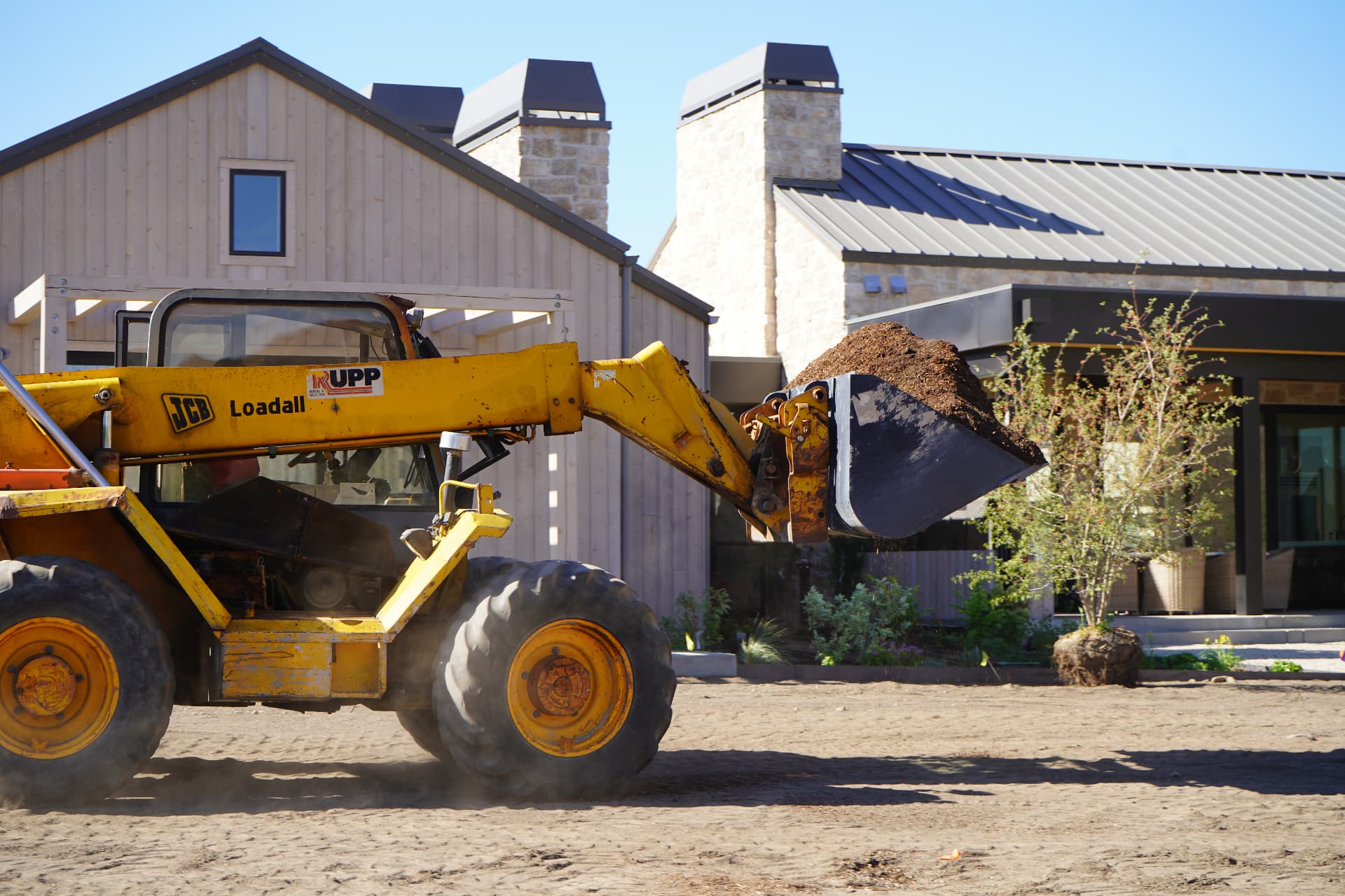 Yellow JCB Loadall moving mulch at a large landscaping project