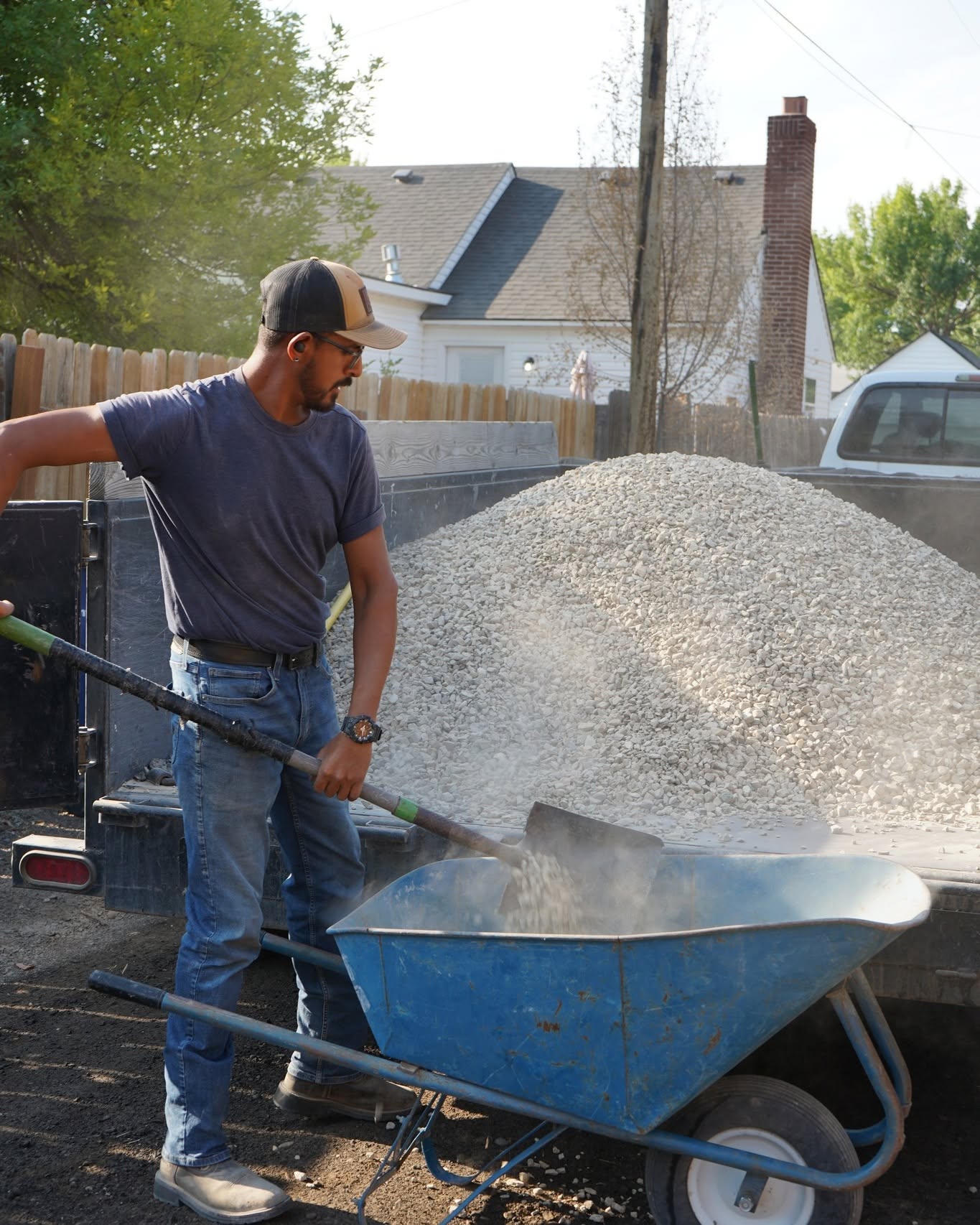 Worker shoveling white gravel into a wheelbarrow for a landscaping project