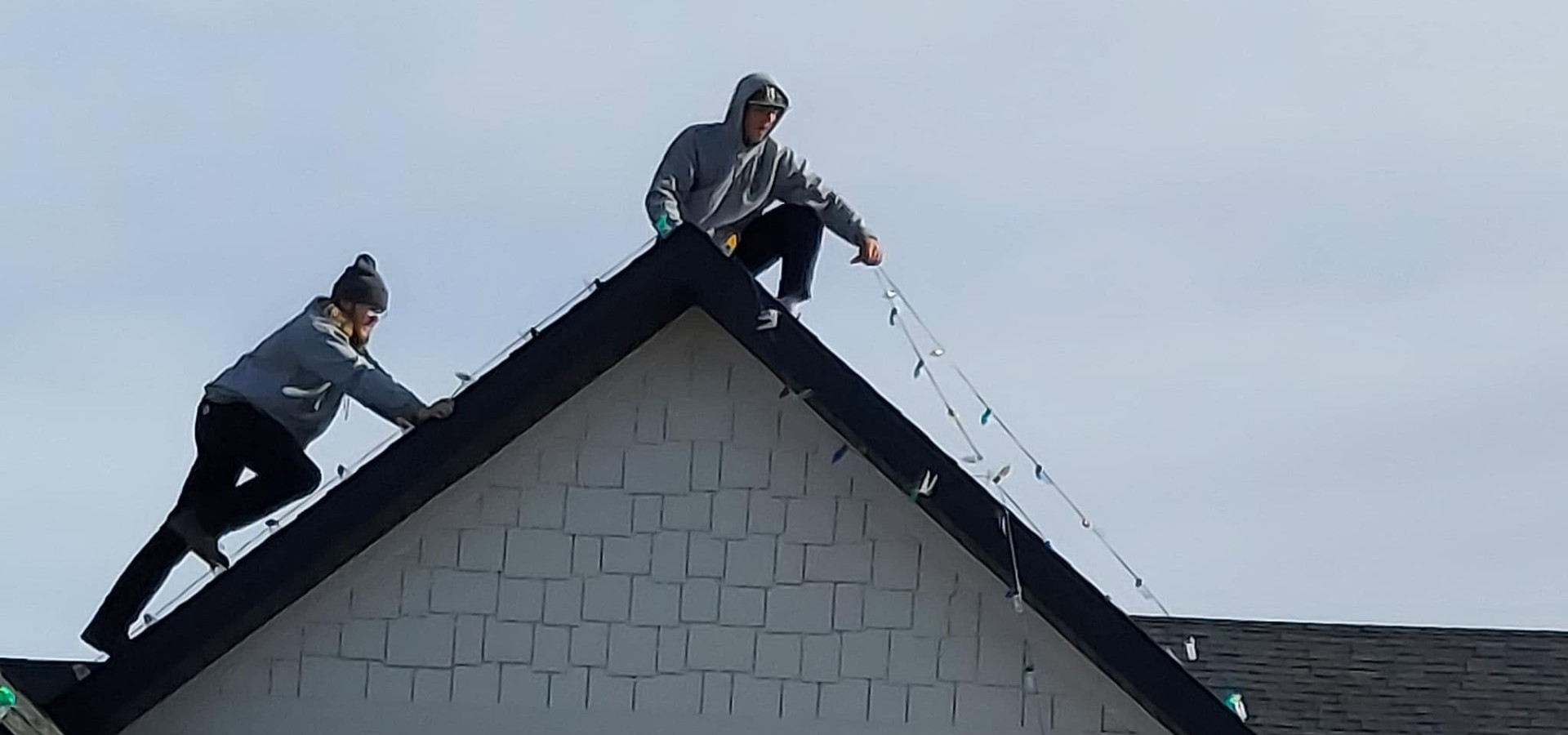 Technicians carefully installing Christmas lights along a roofline