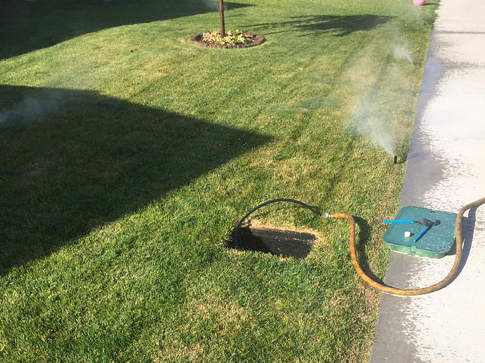 landscaping irrigation control panel open with a hose connected to blow out sprinkler system