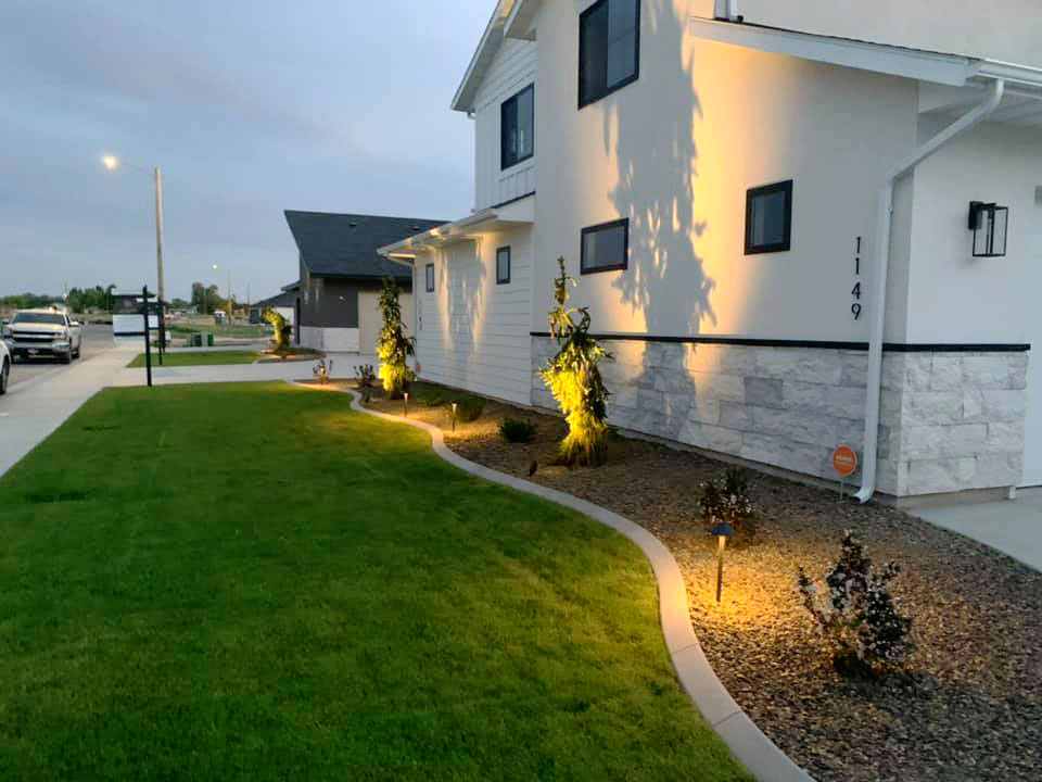 front of a house with new landscaping and curbing with landscape lighting shining onto the house and plants